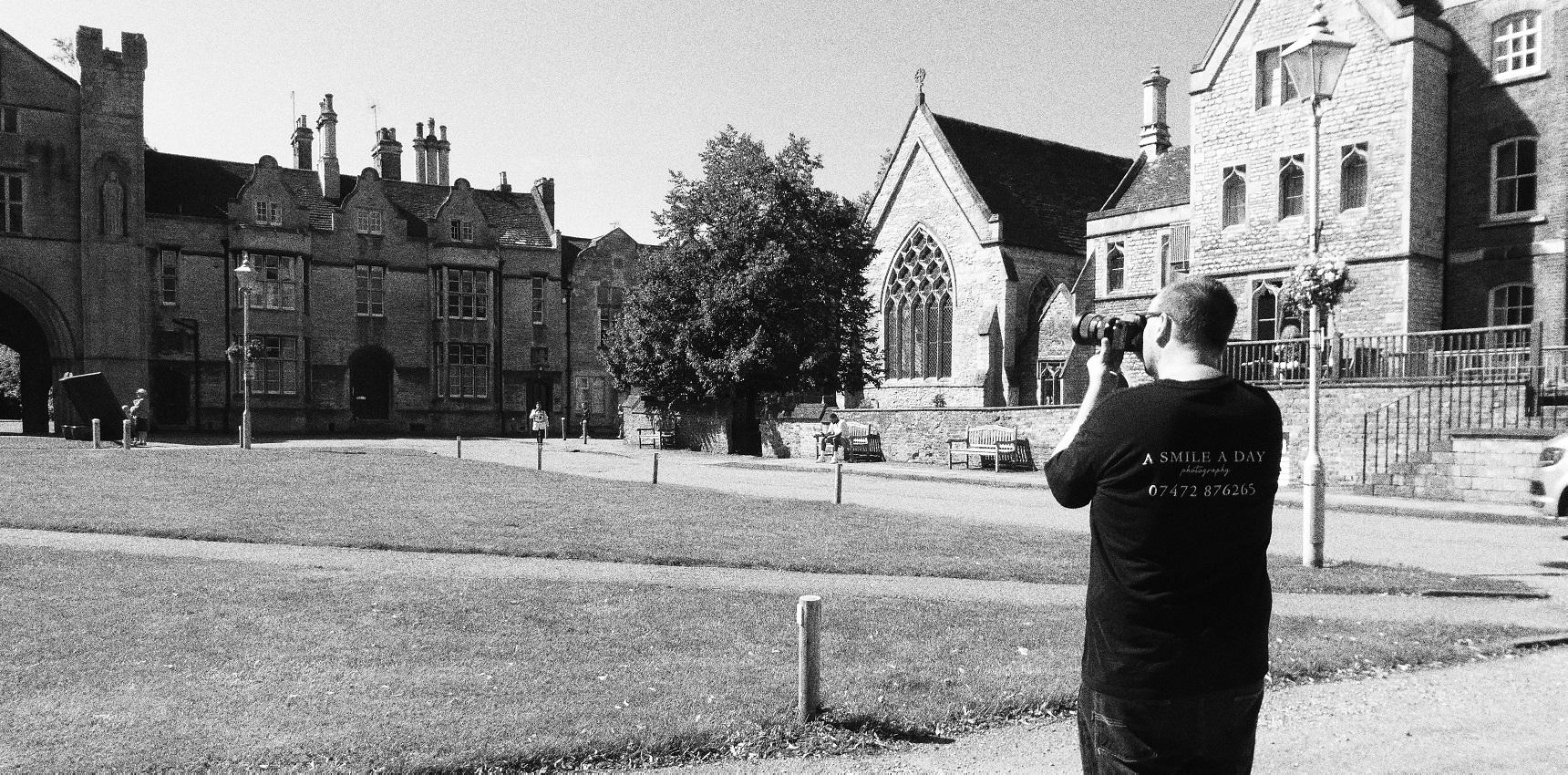 Photographer Nate Landsell, stands in front of a large building taking a shot of it.