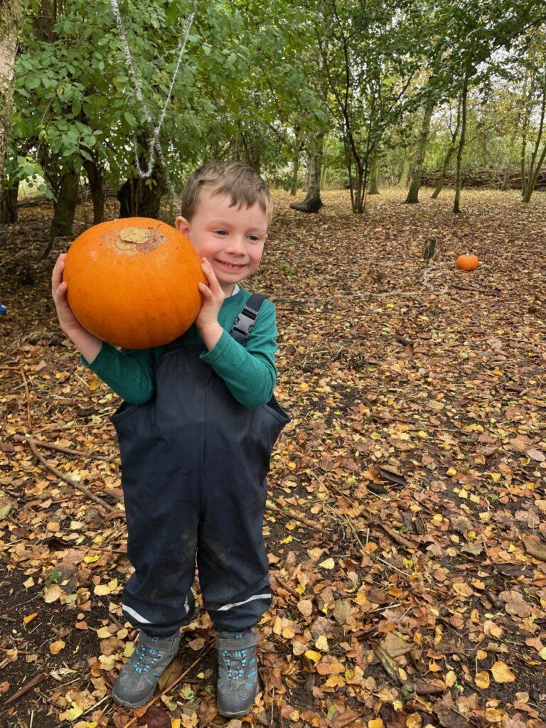 A small child is holding a large pumpkin, with a smile on his face.
